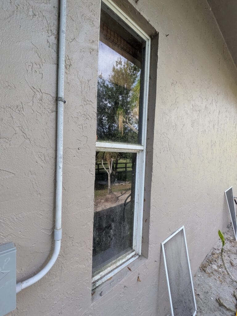 Exterior residential window with screens removed beside a stucco wall